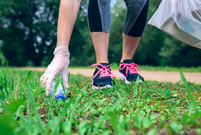 personne en tenue de sport qui ramasse une bouteille plastique