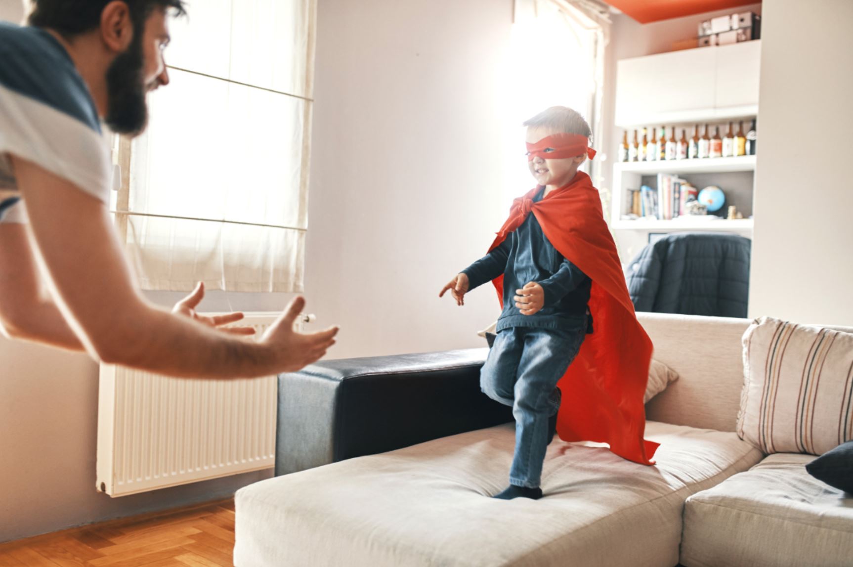 un enfant déguisé en super héro saute dans les bras de son père depuis un canapé
